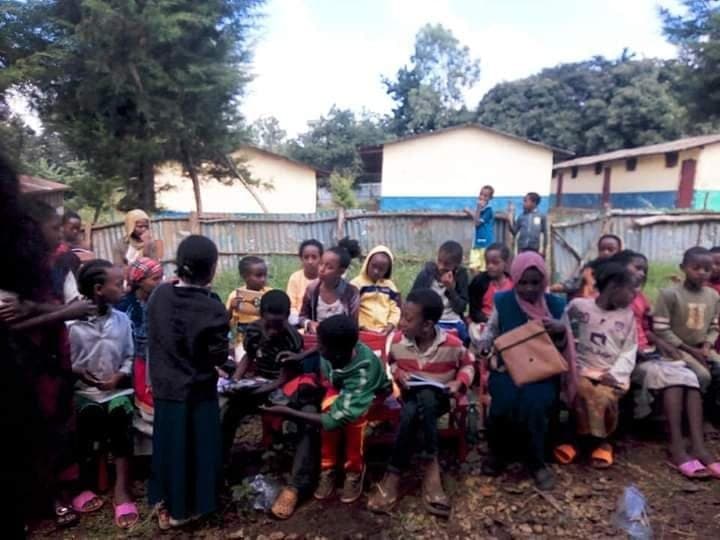 Children sitting outdoors with volunteers and books