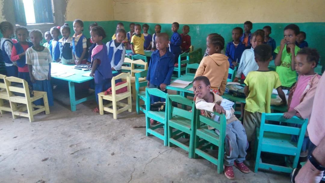 Kindergarten children standing in a classroom with small green chairs