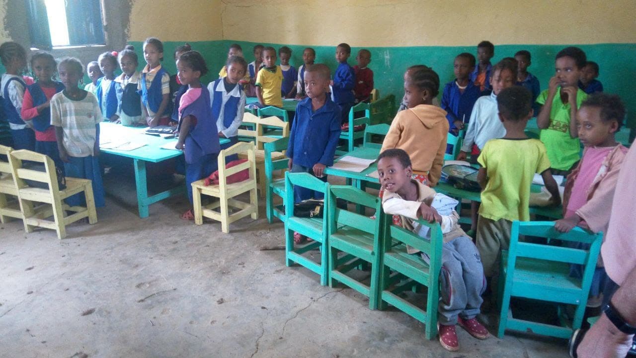 Kindergarten children standing in a classroom with small green chairs