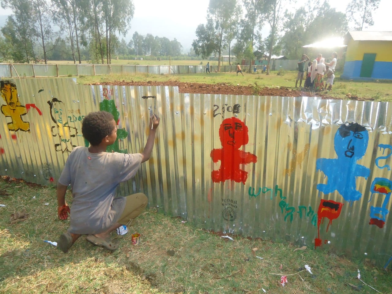 A boy painting a figure on the fence